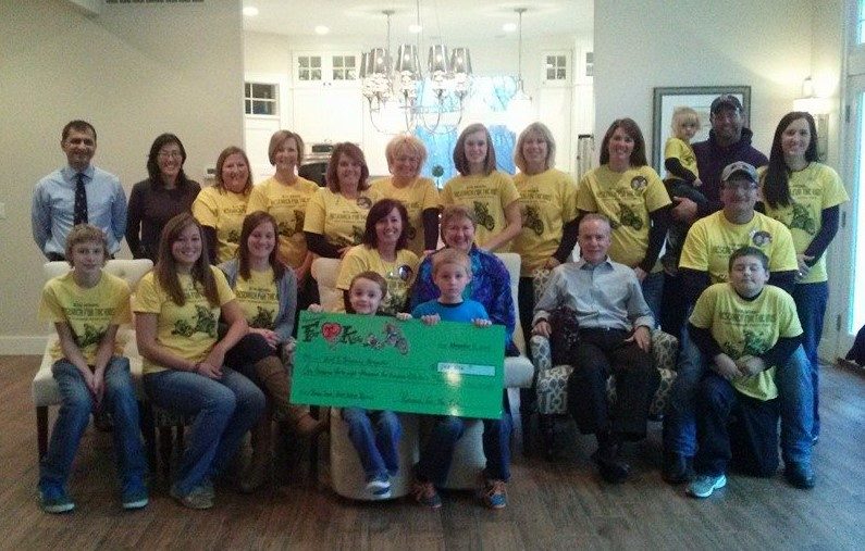 The committee in yellow shirts seated around a handmade check in a living room