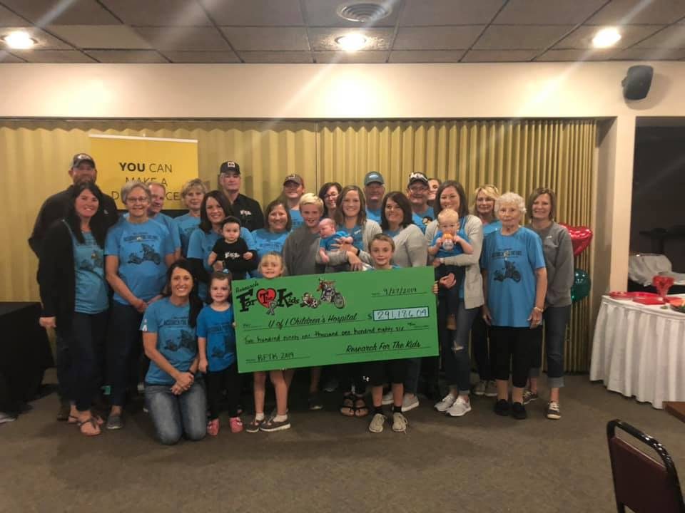 A large group in blue Research For The Kids shirts holding a $291,186.04 check