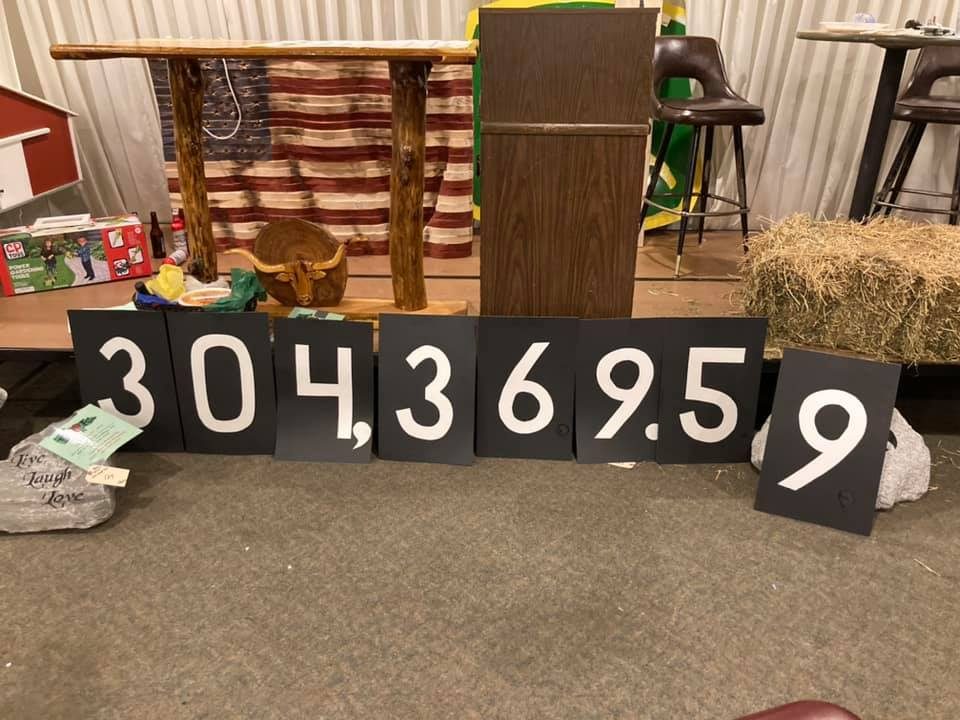 Volunteers on a hall floor holding black cards with white numerals spelling out the year's total