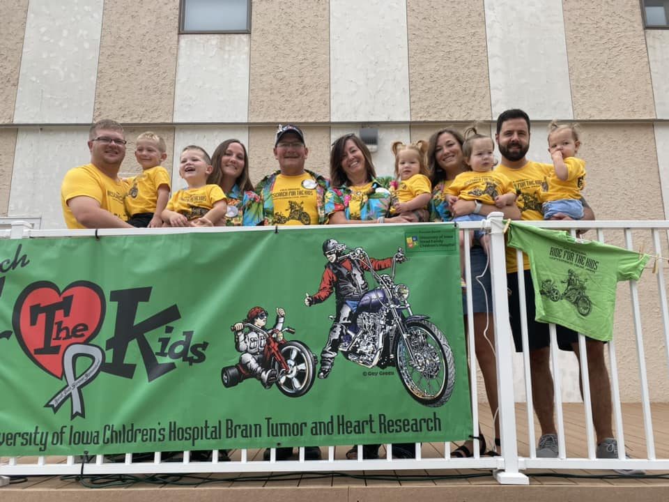 Three generations of the family in yellow shirts behind the Research For The Kids banner